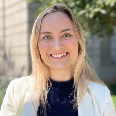 Melody is seen smiling with a white blazer and blonde hair