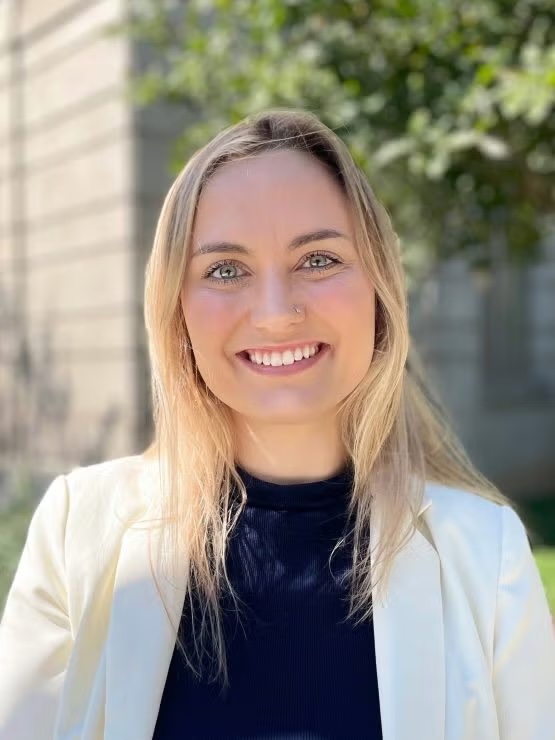 Melody is seen smiling with a white blazer and blonde hair