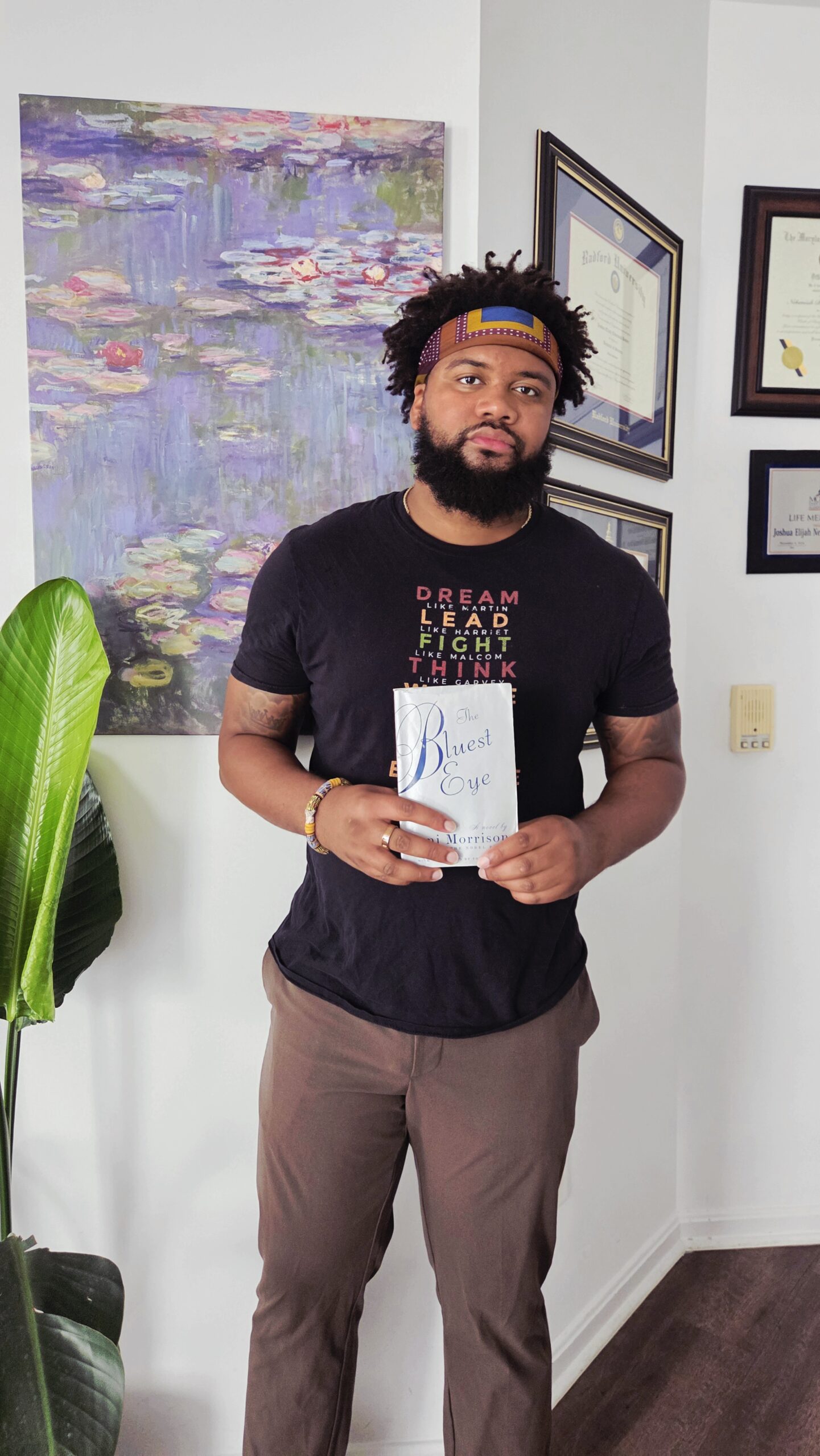 Nehemiah holds the book the Bluest Eye in a Black t-shirt