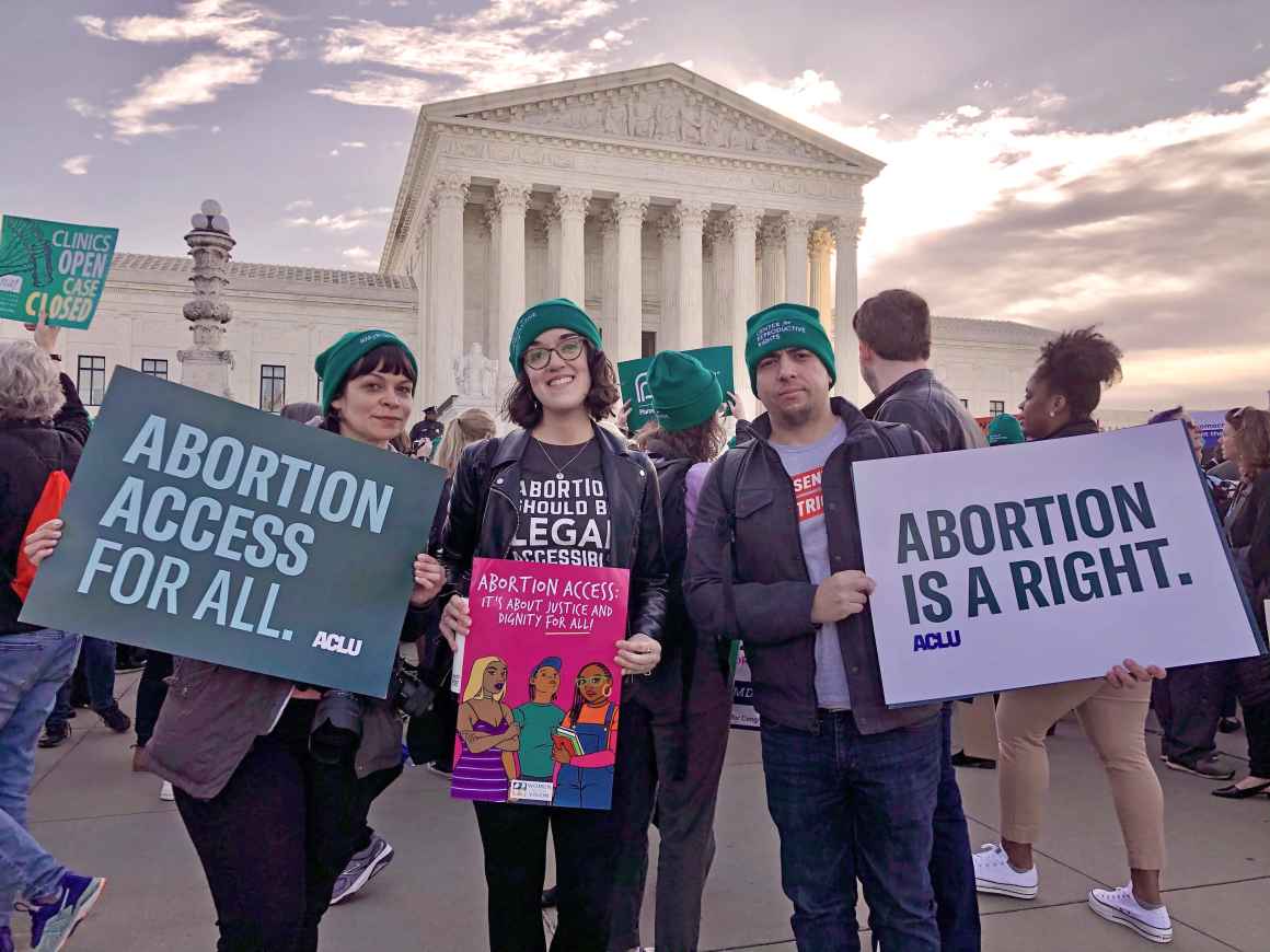 ACLU staff members Nicole McCann on the left and Sergio España on the right hold signs that say Abortion Access for All and Aboriton is a Right. They are in front of the Supreme Court for an abortion rights rally.