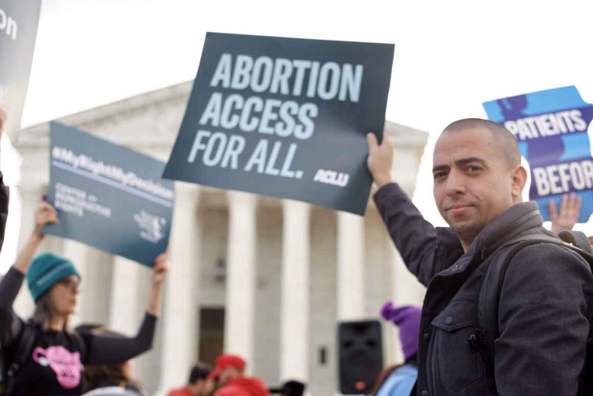 At an abortion rights rally, Sergio España holds an ACLU sign that says Abortion Access for All in front of the Supreme Court of the United States.