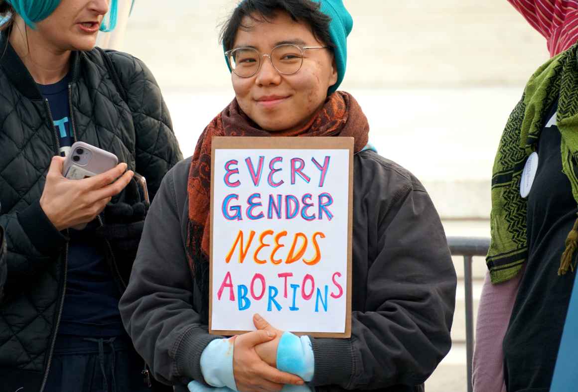 A person holds a sign that says Every Gender Needs Abortion.