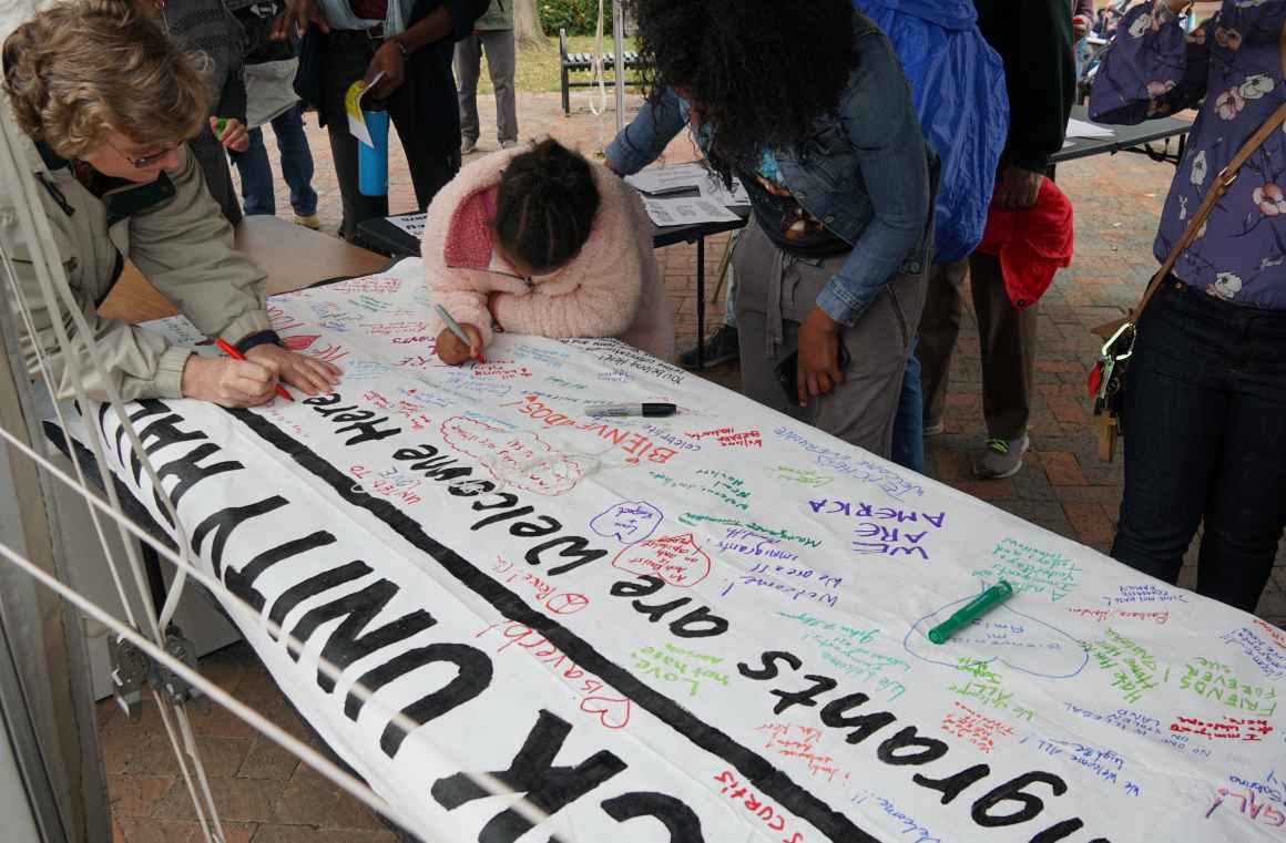 Frederick Unity Rally attendees write messages on Immigrants Welcome Here banner