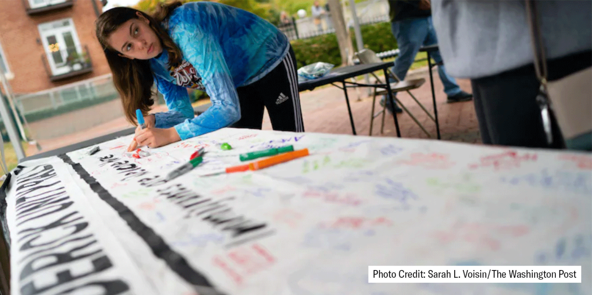 Person is writing on a banner on a table. Photo Credit: Sarah L. Voisin/The Washington Post