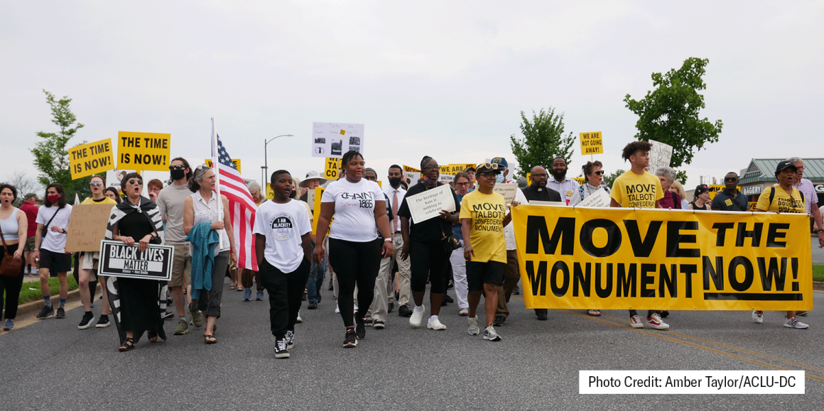 Move the Monument rally photo of a group marching down the street with a yellow banner. Photo credit: Amber Taylor.
