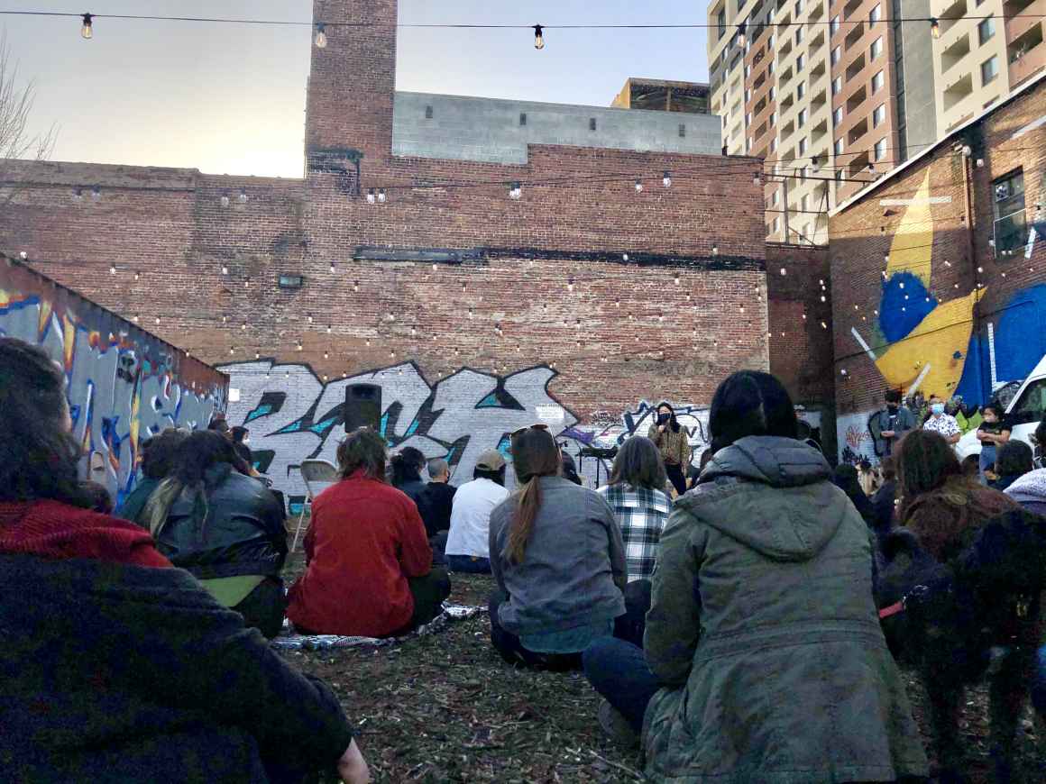 People sit on the ground listening to a speaker at the vigil at the YNot Lot in Baltimore for the victims of the shooting in Atlanta, GA. Asian people in Baltimore spoke about their own experiences.