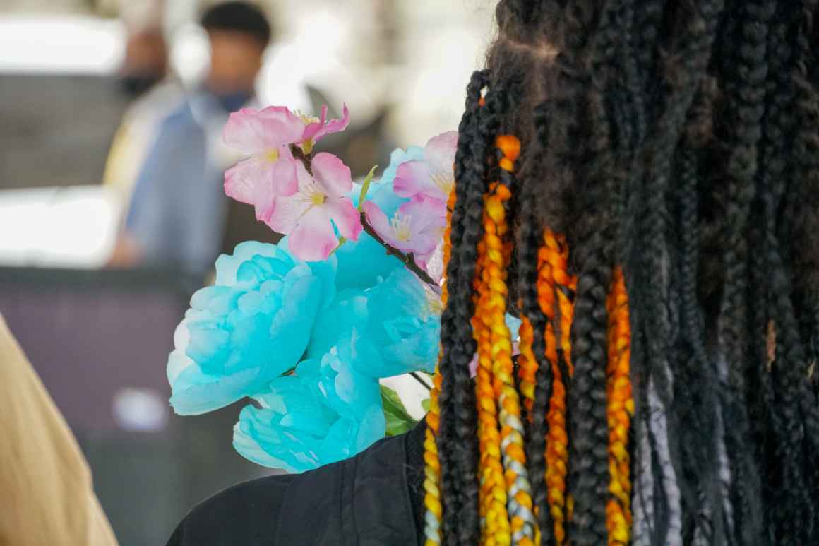 Blue, pink, and white flowers representing the trans flag, and a Black person's braids with orange and yellow accents.
