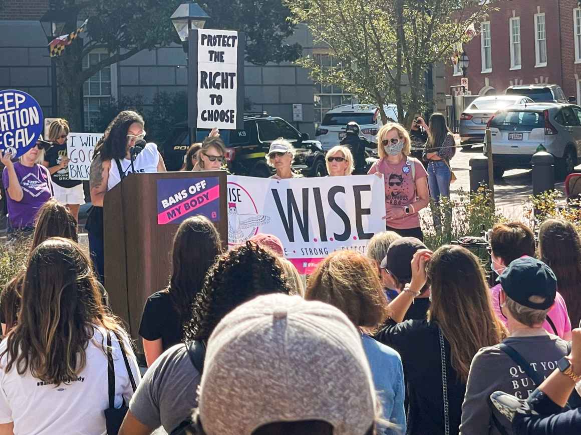 Ashley Esopsito speaks at an abortion access rally in Annapolis, MD. She is a Black woman standing at a podium with people standing in Lawyer's Mall.