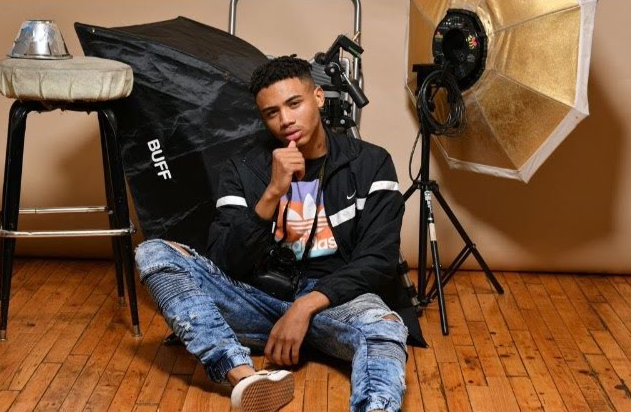 Anton Black is sitting on the hardwood floor and has photoshoot lights around him.