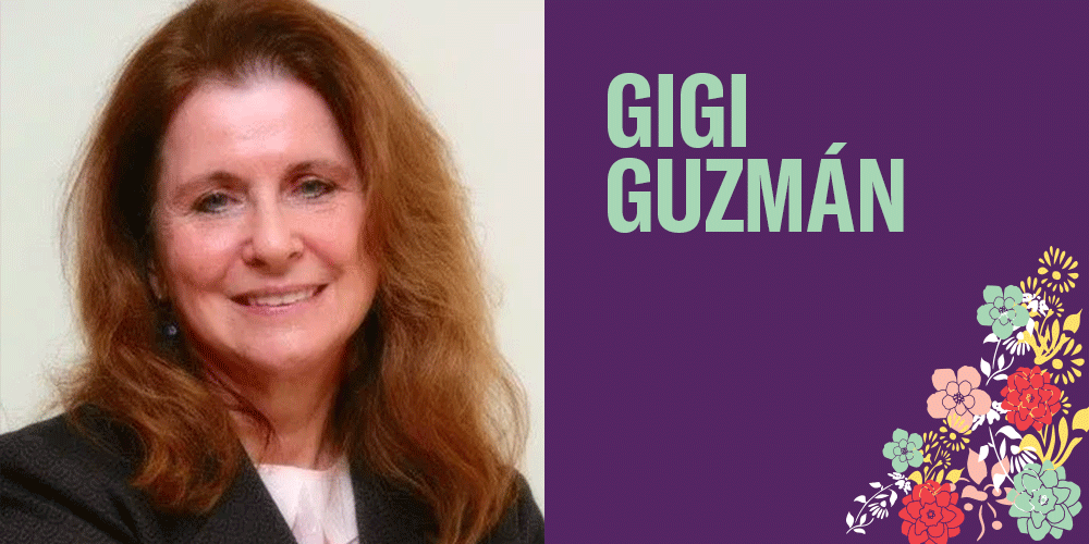 Gigi Guzmán has a long red auburn hair, light beige skin otne and is smiling at the camera. There are bright colorful flowers in the bottom right corner.