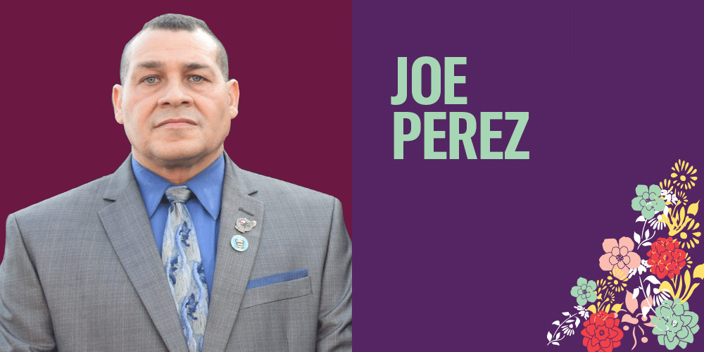 Joe Perez is a Latino man with short hair. He is wearing a light suit and tie. There are bright flowers in the bottom right corner.