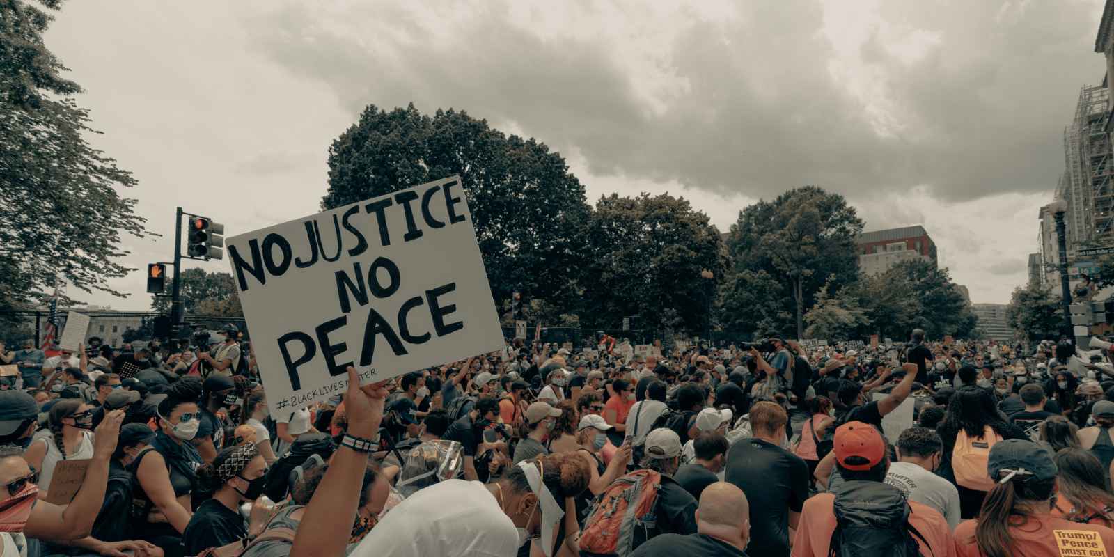 Group of people outside at a protest. Someone is holding a sign that says, "No Justice, No Peace."