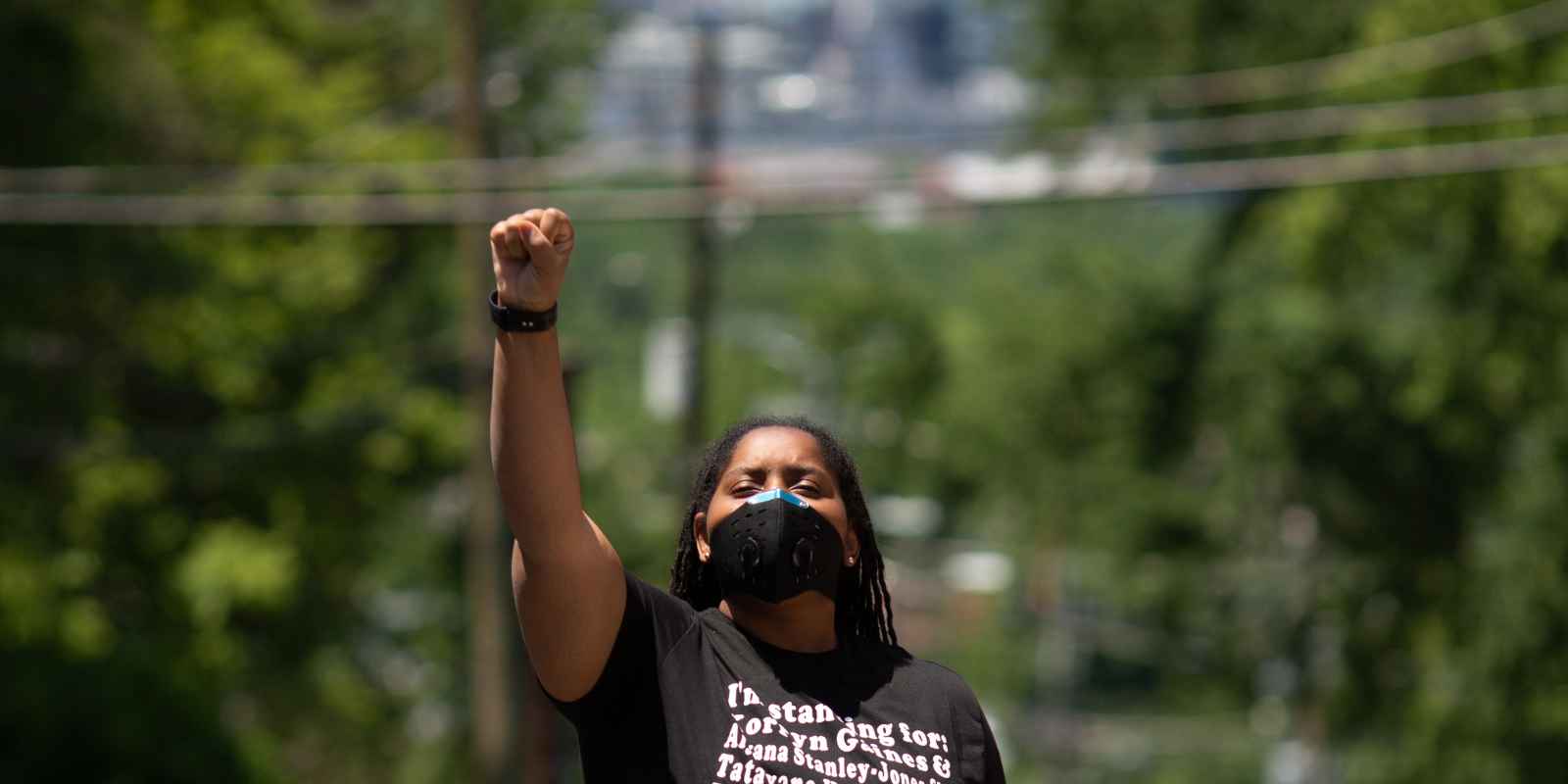 Black person with fist in the air wearing a t-shirt with the names of Black people killed by police