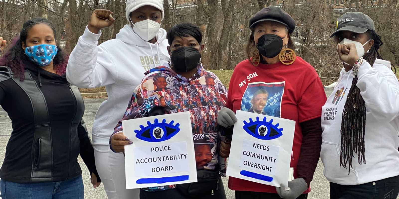 A group of Black and Residents of Color who are also advocates in Prince George's County are standing together. Two have their fists raised and two are holding signs that say "Police Accountability Board." Photo by Sergio España.