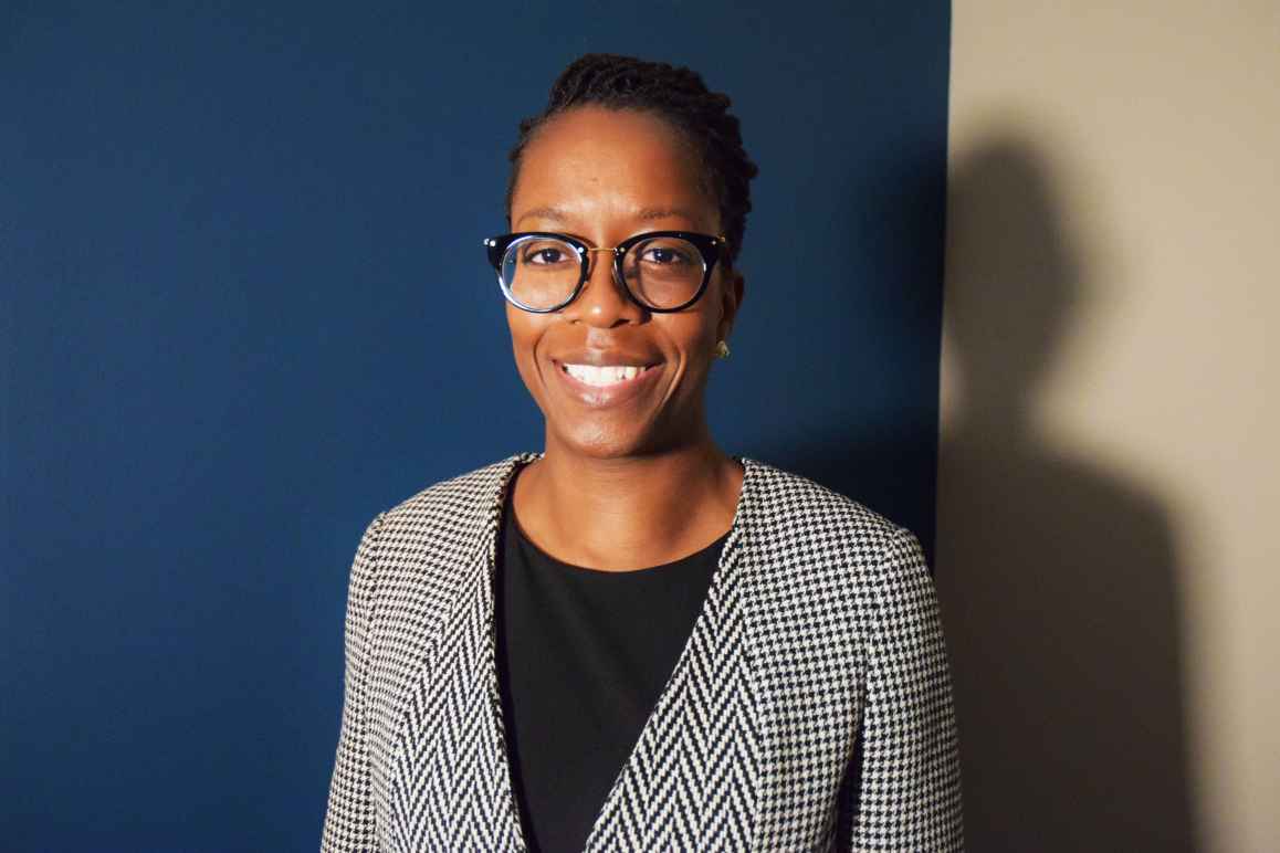 Boatemaa Ntiri, a Black woman, shirt hair, wearing glasses and a herringbone jacket and black shirt