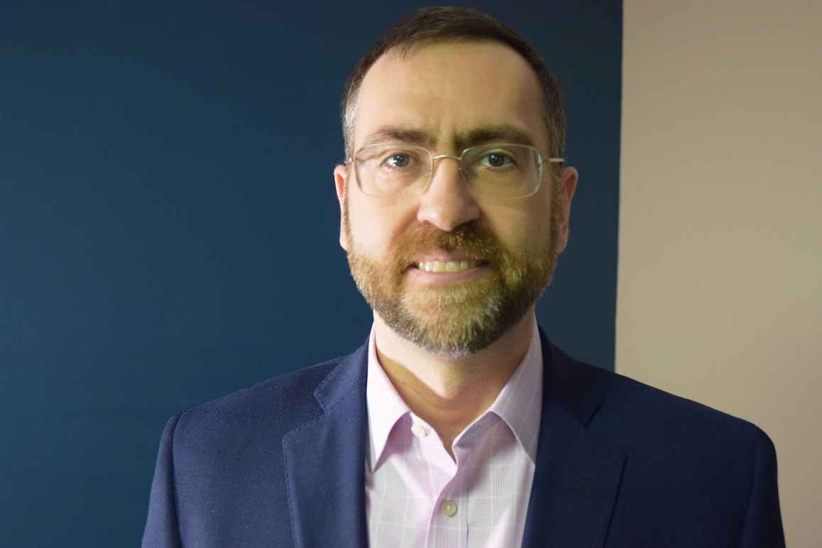 Corey Stottlemyer, white man, wearing glasses, short bard, navy blue suit jacket with light colored collared shirt