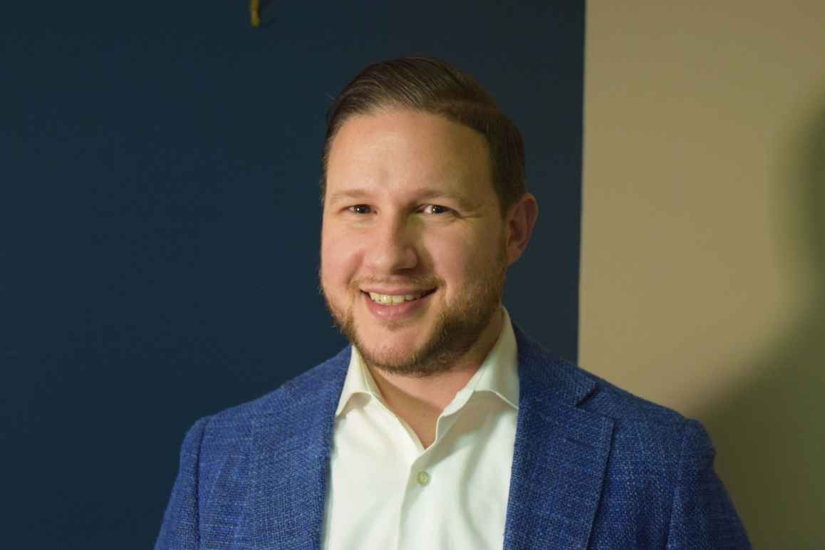 Eric Gillman, white man, wearing blue suit jacket, light yellow collared shirt