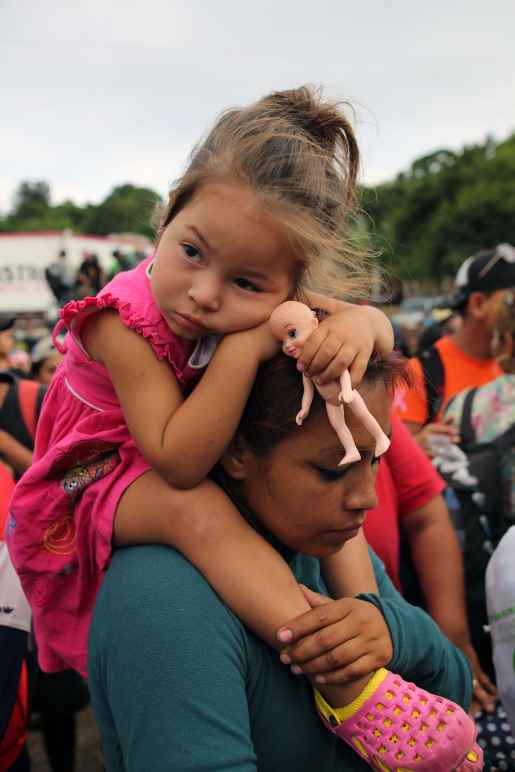 Immigrant family, child is sitting on parent's shoulders with a doll in her hands.