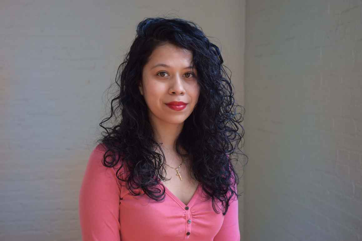 Smiling person with pink shirt, a necklace cross, and long black hair. 