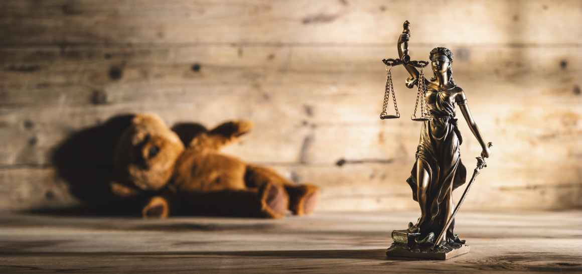 Image shows justice scales and statue and a teddy bear laying on its side.