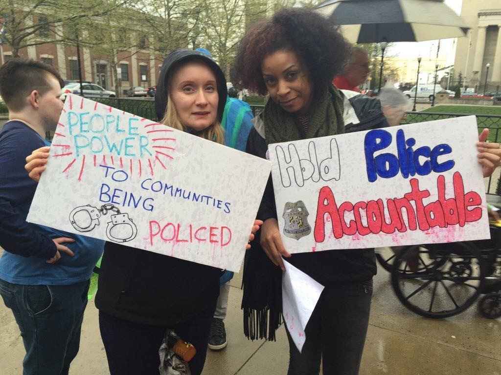Two women at a rally with signs calling for "People Power to the Communities being Policed" and "Hold Police Accountable"