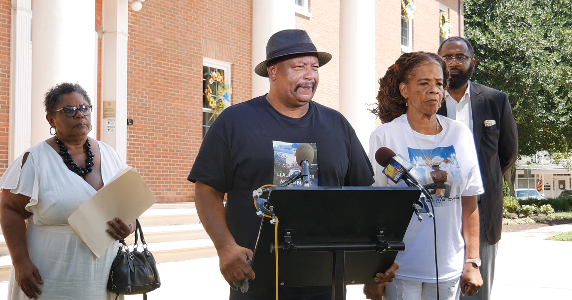 Anton Black's family and members of the Coalition for Justice for Anton Black are outside at a podium for a press conference. There are two Black women and two Black men pictured. 