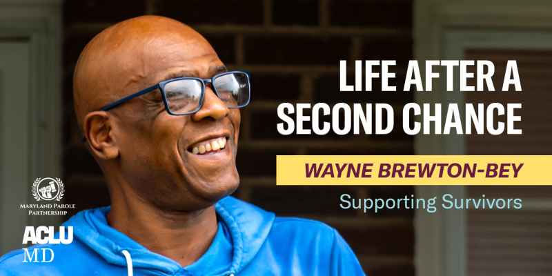 Wayne Brewton-Bey is a Black man with warm medium-brown skin tone, has shaved head, is wearing glasses, and is smiling. He is standing outside on a front porch.