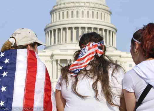 Three people are facing the US Capitol Building with American flags