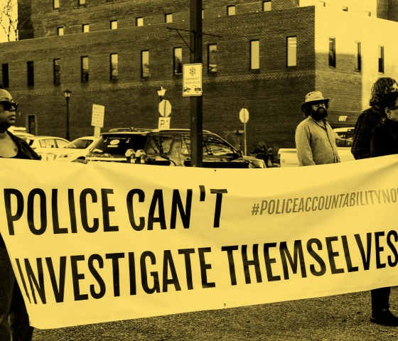 Photo of two Black advocates holding a banner that says, "Police can't investigate themselves." The image has a black and yellow gradient filter.